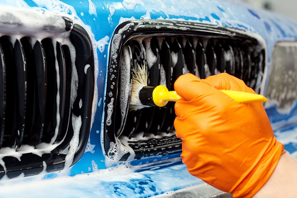 hand using brush to clean car grill